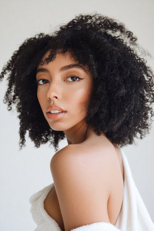 A young model showcases her natural beauty with voluminous curly hair in a well-lit studio. Soft lighting highlights her features, creating an inviting atmosphere.の素材