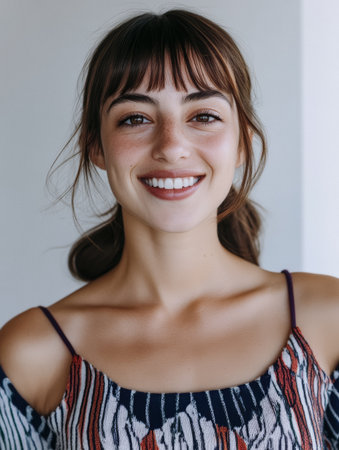 A young woman smiles brightly while standing indoors in a modern environment. She wears a stylish, colorful top. The natural lighting highlights her cheerful expression and beauty.の素材