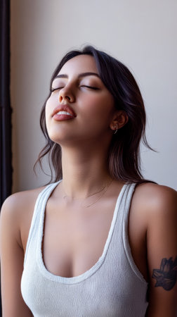 A young woman sits with her eyes closed in a bright, sunlit room, embodying tranquility and mindfulness. Her casual attire complements the serene atmosphere.の素材
