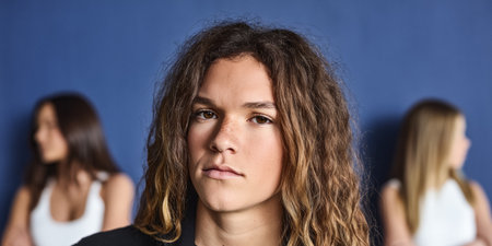 A young individual with curly hair stands prominently in the foreground, showcasing self-assurance. Two people with straight hair sit in the background, creating an interesting contrast.の素材