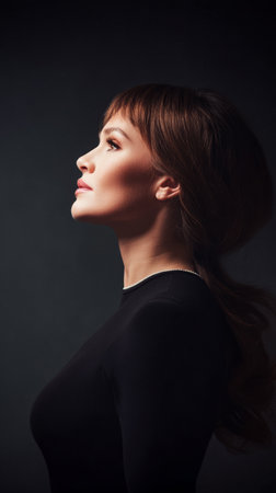 A woman strikes a confident pose, her side profile illuminated by soft light. The dark background emphasizes her features, creating a stylish and artistic atmosphere.の素材