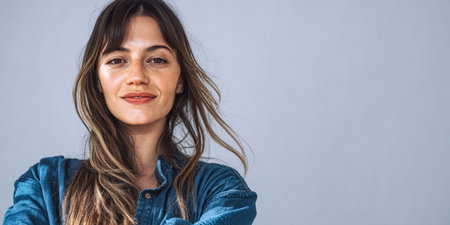 A woman stands with her arms crossed, wearing a blue shirt. She has long, flowing hair and a warm smile, creating an inviting atmosphere in a well-lit indoor space during daytime.の素材