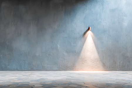 A spotlight shines down on a smooth stone floor, highlighting a textured blue wall. The room is empty and reflects a calm, minimalistic atmosphere.の素材