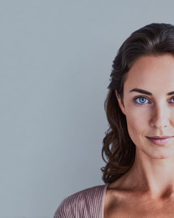 A woman with striking blue eyes and soft wavy hair looks directly at the viewer. She has a serene expression, and the soft light highlights her features, creating an elegant atmosphere.の素材