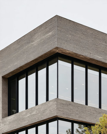 This structure displays a unique textured exterior with a modern design. Large glass windows reflect daylight, showing an urban environment surrounded by greenery.の素材