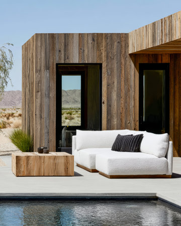 A stylish outdoor lounge features a white sectional sofa and a wooden coffee table, set against a backdrop of desert hills and a serene swimming pool.の素材