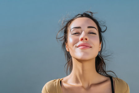 A cheerful woman enjoys a sunny day by the ocean, smiling brightly as the wind plays with her hair. She stands against a backdrop of clear blue sky and calm waters.の素材