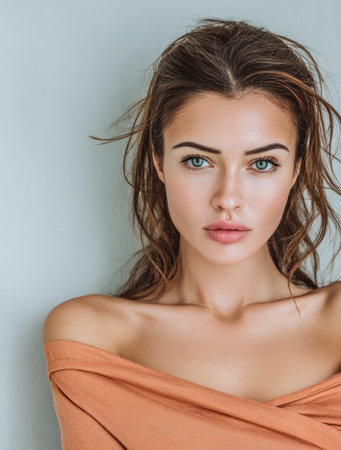 A young woman with beautiful green eyes stares confidently at the viewer. Her hair is tousled, and she wears a warm-toned off-shoulder top. The background is neutral, enhancing her features.の素材