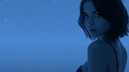 A female model stands gracefully in soft blue light, creating a serene atmosphere. Her expression is confident, captivating, and full of intrigue during the photoshoot.の素材