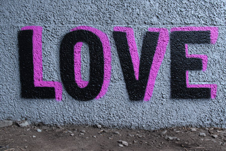 Colorful graffiti featuring the word LOVE in bold letters is painted on a textured urban wall. The artwork adds character and a positive message to the surrounding area.の素材