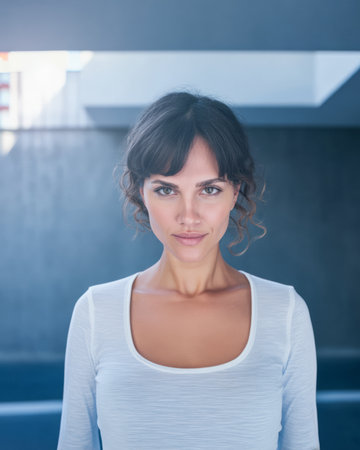 A woman stands confidently in a contemporary space with soft daylight illuminating her features. She looks directly at the viewer with a calm expression.の素材