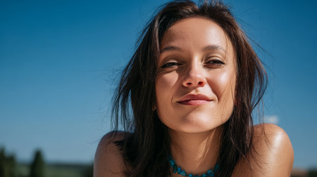 A woman with brown hair smiles brightly while enjoying a sunny day outside. The clear blue sky highlights her joyful expression and relaxed atmosphere among nature.の素材