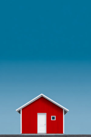 A bright red house with a white door sits in an open area, surrounded by a clear blue sky, creating a peaceful and serene rural atmosphere.の素材