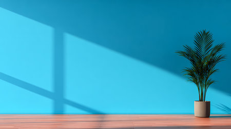 A vibrant room features a smooth blue wall and a healthy green plant in a simple pot on warm wooden flooring. Sunlight creates beautiful shadows on the wall.の素材