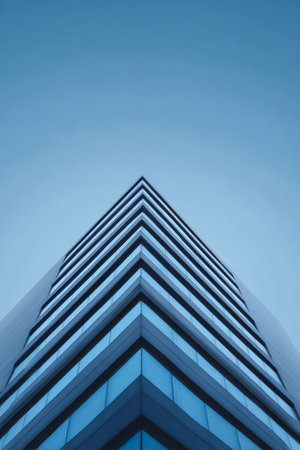 The striking symmetry of a high-rise building, with its sleek glass facade and layered design reaching towards a bright blue sky.の素材