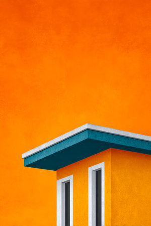 A vibrant orange wall stands behind a modern building topped with a blue roof. The white-framed windows create a striking contrast, showcasing a minimalistic design.の素材