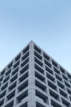 A contemporary concrete structure stands tall against a clear blue sky. The building features a geometric design with repeating patterns of windows, showcasing urban architecture.の素材