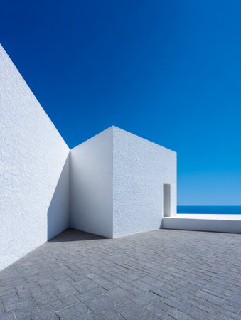 A minimalist architectural space showcases stark white walls and angular shapes, surrounded by a clear blue sky and calm ocean. The scene conveys tranquility and simplicity.の素材