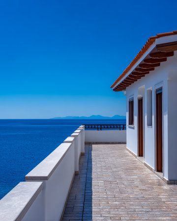 A bright terrace features white walls and wooden accents, offering a mesmerizing view of the calm blue sea and distant islands under a cloudless sky, perfect for relaxation.の素材