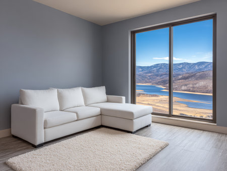 Bright living room features a cozy white couch with a scenic view of mountains and a serene lake through large windows in daytime light.の素材