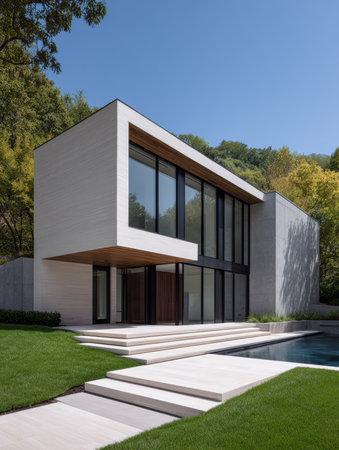 A contemporary house features large glass windows and clean lines. It sits beside a swimming pool with steps leading up to a well-maintained lawn. The bright sky enhances the sleek design.の素材
