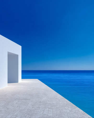 A simple white building stands on a stone path leading to tranquil blue waters. The clear, bright sky reflects the peacefulness of this coastal scene during midday.の素材