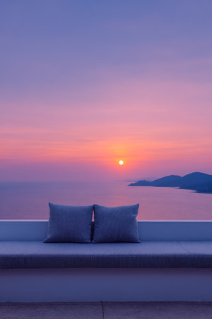 A stunning sunset casts vibrant colors over the ocean while two cushions rest on a seating area, offering a perfect spot to relax and enjoy the view in peace.の素材
