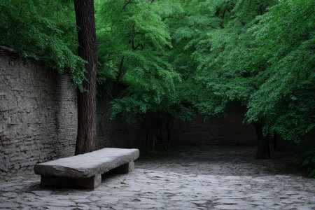 A large stone bench rests quietly in a lush green garden. Surrounding trees and walls create a serene atmosphere, perfect for relaxation or contemplation.の素材