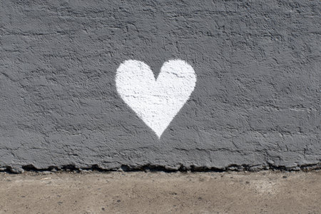 A small white heart is painted on a rough gray wall, highlighting urban creativity. The heart stands out against the muted background, bringing joy and art to the space.の素材