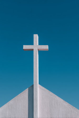 A bright white cross stands tall against a blue sky, located on the roof of a church during the daytime. The scene conveys a sense of peace and spirituality.の素材