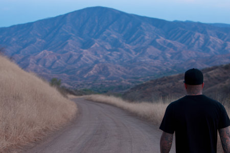 A person stands on a dirt road surrounded by mountain scenery at dusk. The mountains are partially visible, showcasing their natural beauty and rugged terrain.の素材