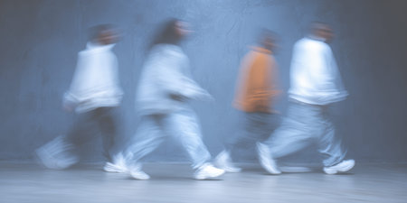 Four individuals walk in a blurred motion across a gray studio space. Their casual outfits and movement create a sense of dynamism and rhythm in the environment.の素材