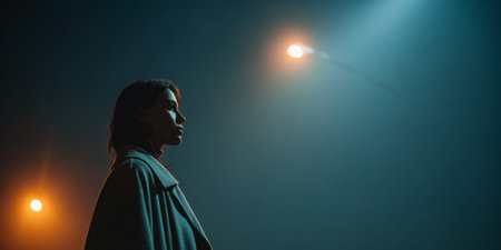A woman stands quietly in a dark setting, illuminated by blue and orange lights. She appears reflective and contemplative, enhancing the artistic atmosphere of the venue.の素材