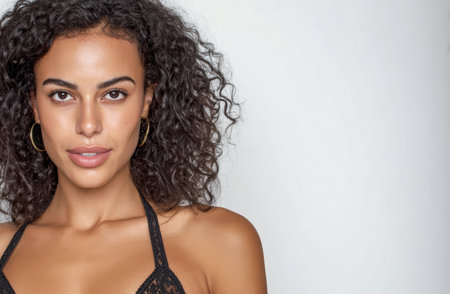 A woman with curly hair showcases her confidence while posing in a black lace outfit. The neutral background emphasizes her natural beauty and graceful presence.の素材