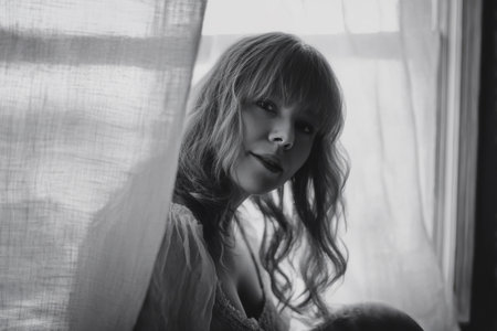 A woman is seated by a window, surrounded by sheer curtains. She gazes into the room, lost in thought. Soft light fills the space as time passes in the afternoon.の素材