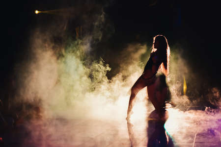 silhouette of a woman dancing between lights and smokeの写真素材