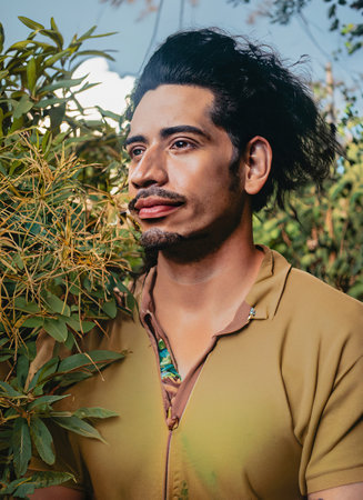 Attractive young man with tousled black hair, surrounded by lush vegetation. Offbeat portraitの素材