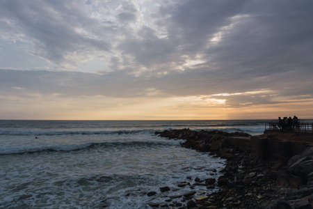 Beautiful sunset in Lima Peru, bright sky and underexposed beach, golden hour, orange sky, rock piles into the seaの写真素材