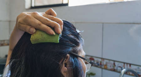 unrecognizable adult woman spreading aloe cortex on her hair in a kitchen with unfocused faucet kitchen and tiles backgroundの写真素材