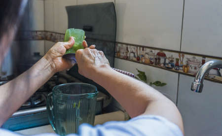 Unrecognizable adult woman pouring aloe gel into a blender jar with a spoon in a kitchenの写真素材