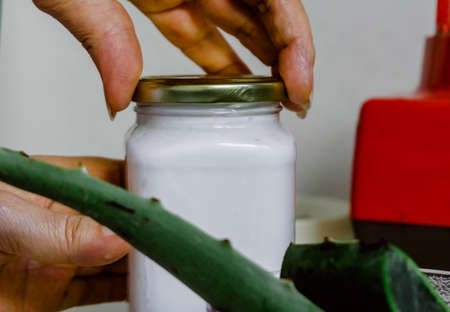 woman hands putting on the cap of a little glass jar full of aloe gel juice. Aloe leaf in a glass bowl and red blenderの写真素材