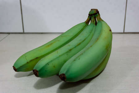Green complete bananas on a kitchen table with unfocused backgroundの写真素材