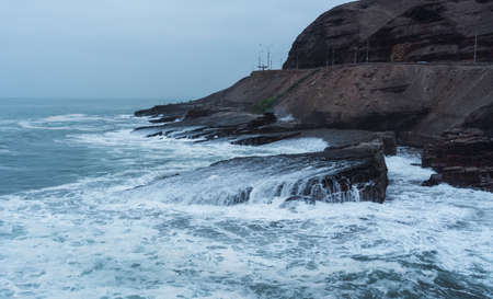 Coast line in Chorrillos Lima Peru, waves splashing and hitting rocks in La Herradura beach in a cloudy dayの写真素材