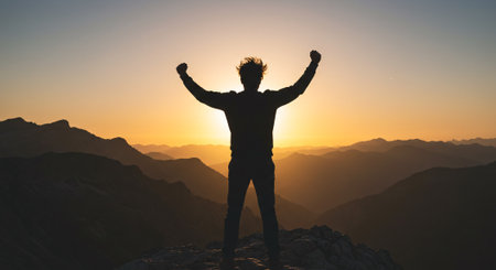 Silhouette of a man standing on the top of a mountain at sunsetの素材