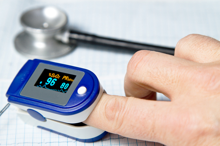 A pulse oximeter used to measure pulse rate and oxygen levels with medical stethoscope and ECG backgroundの写真素材