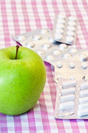 Green apple and pills over a purple tableclothの写真素材