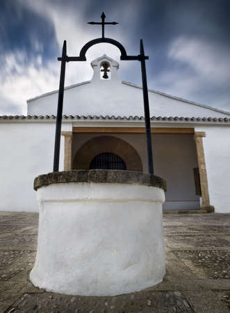 Spanish chapel with a well in the foreground and the church tower in the background. Clouds in motionの写真素材