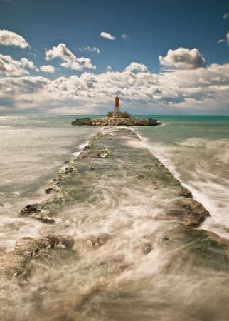 Seascape of a sandy beach with a lighthouse on the background. Vertical composition with a roack as a vanishing pointの写真素材
