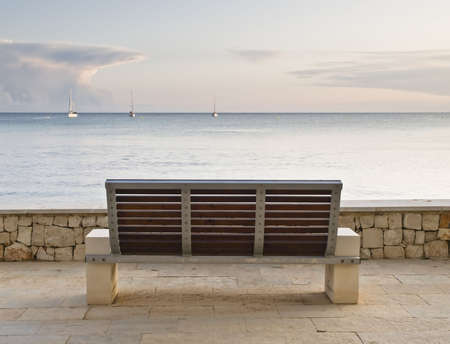 A bench looking to the Mediterranean sea, with some sailboats on the horizon. Image inviting to tranquility and calm の写真素材