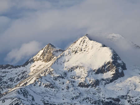 Summit of a snowy mountain surrounded by clouds の写真素材